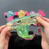 A hand holds a translucent, squishy axolotl stress relief toy with pink and yellow accents.
