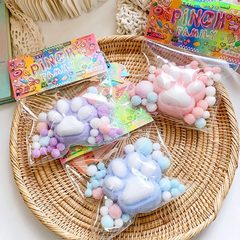 A collection of pink and blue cat paw squishy stress relief toys packaged in clear plastic bags on a woven tray.