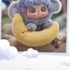 A soft collectible plush doll of a gray animal with blue eyes is resting on a yellow crescent shape.