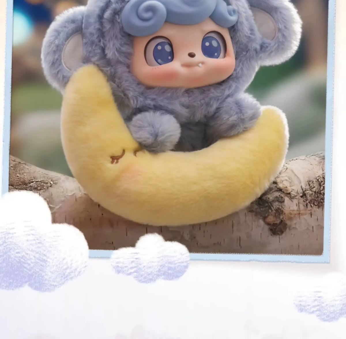 A soft collectible plush doll of a gray animal with blue eyes is resting on a yellow crescent shape.