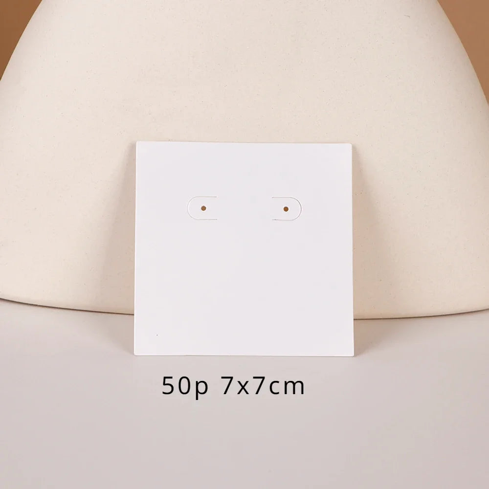 A white square jewelry display card with two small holes is shown against a light beige background.