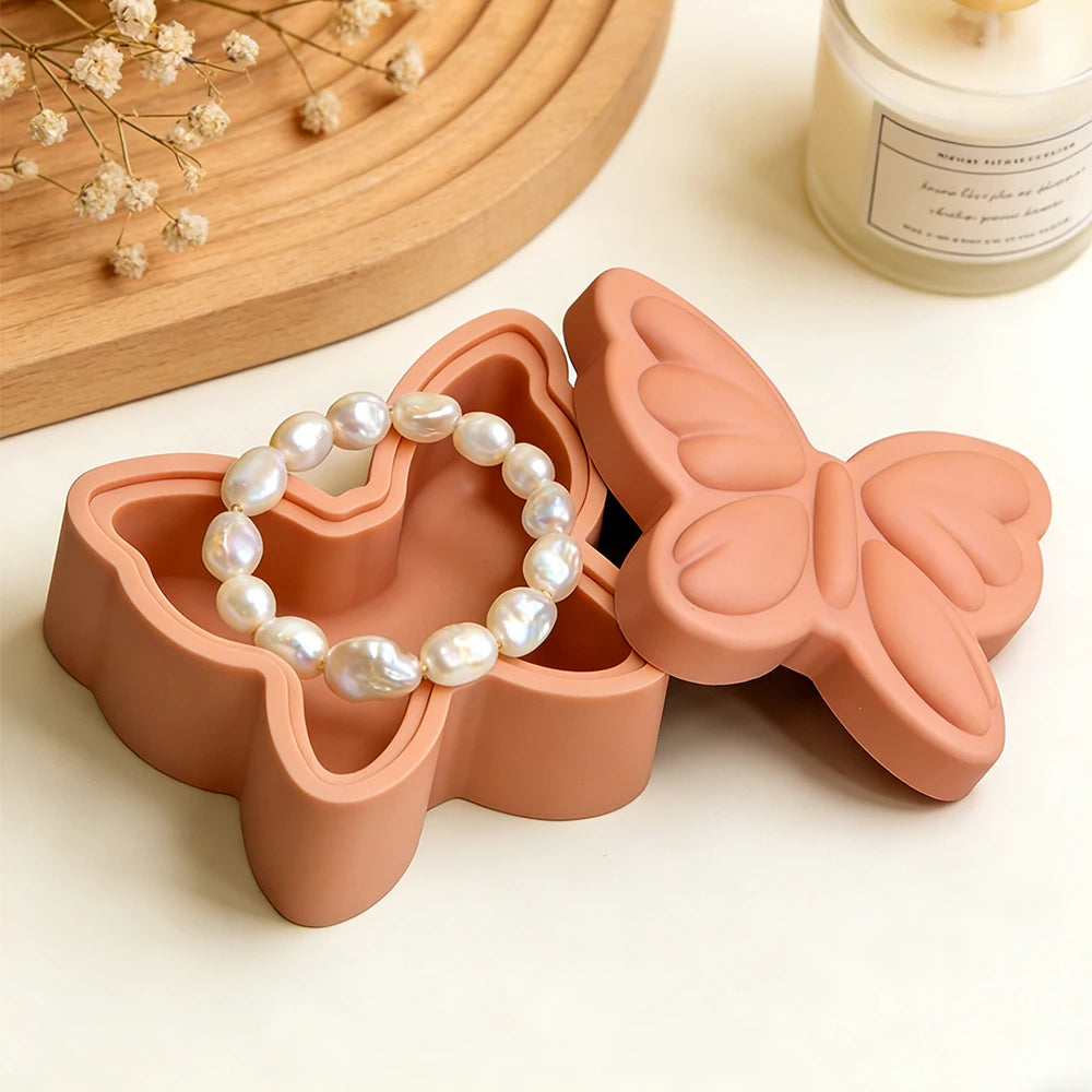 A terracotta silicone resin mold shaped like a butterfly holds a strand of white pearl beads.
