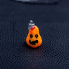 An orange cartoon pumpkin bear figurine with a white stem and red accents, displayed on a dark surface.