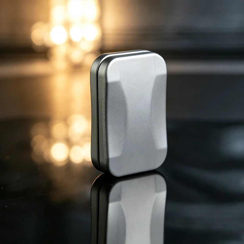 A silver metal fidget slider with a magnetic core is shown on a reflective surface.
