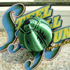 A green steel ball fidget toy with a stylized yellow and blue logo in the background.