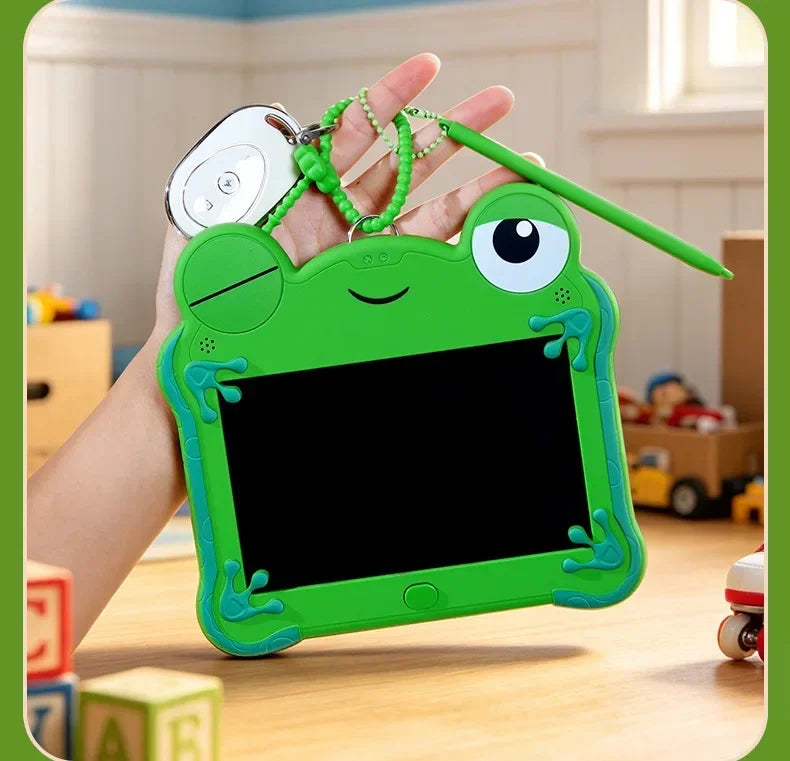 A hand holds a green frog-shaped LCD drawing tablet keychain with a stylus and a clip.