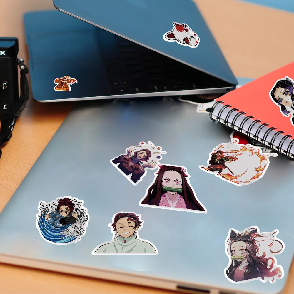 Eine Sammlung von Demon Slayer Anime-Decals auf einem hellblauen Notizbuch und einem dunkelblauen Laptop.