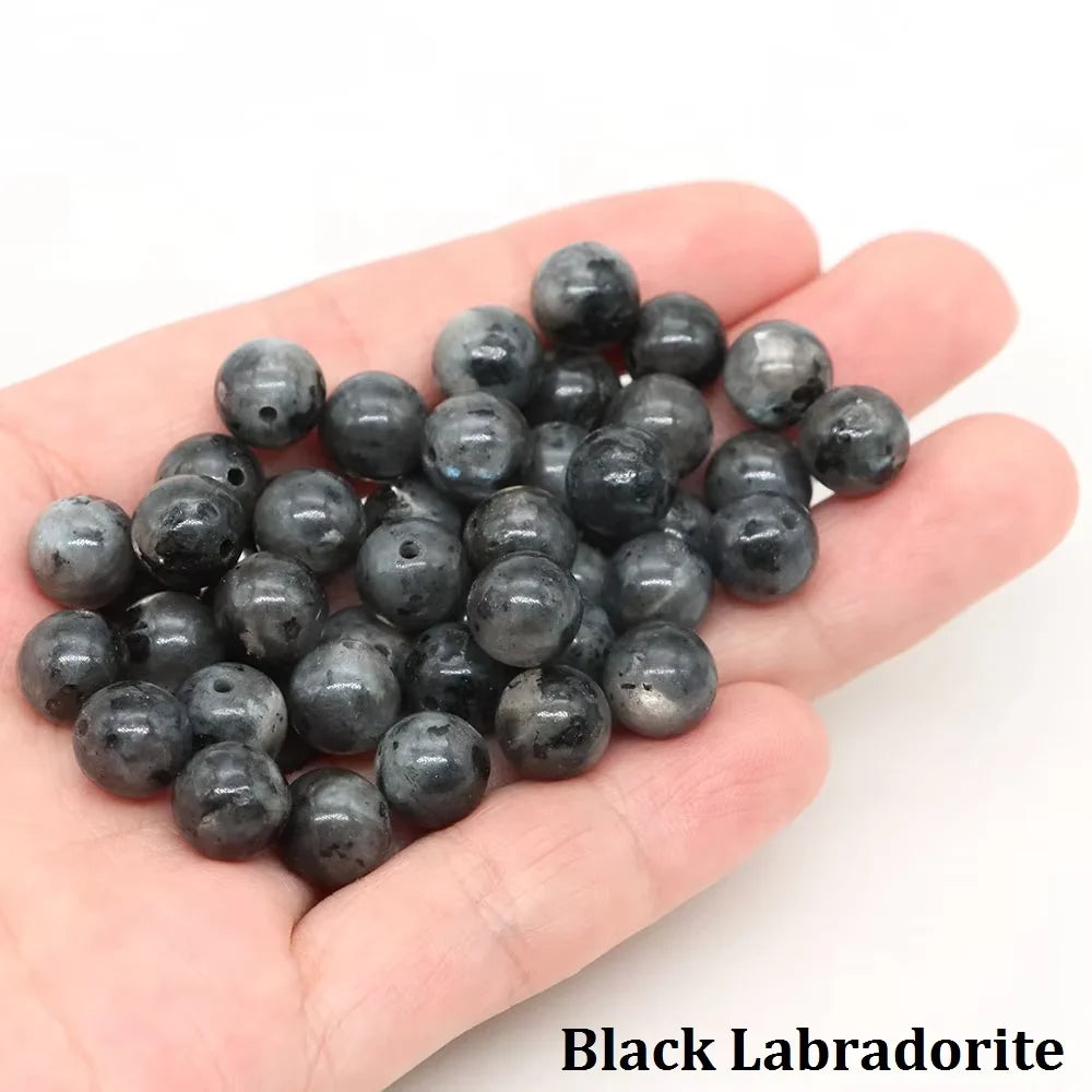 A handful of black labradorite round beads is held in a person's hand.