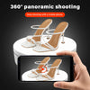 A hand holds a smartphone displaying a 360 degree panoramic shot of white high-heeled shoes on a rotating display stand.