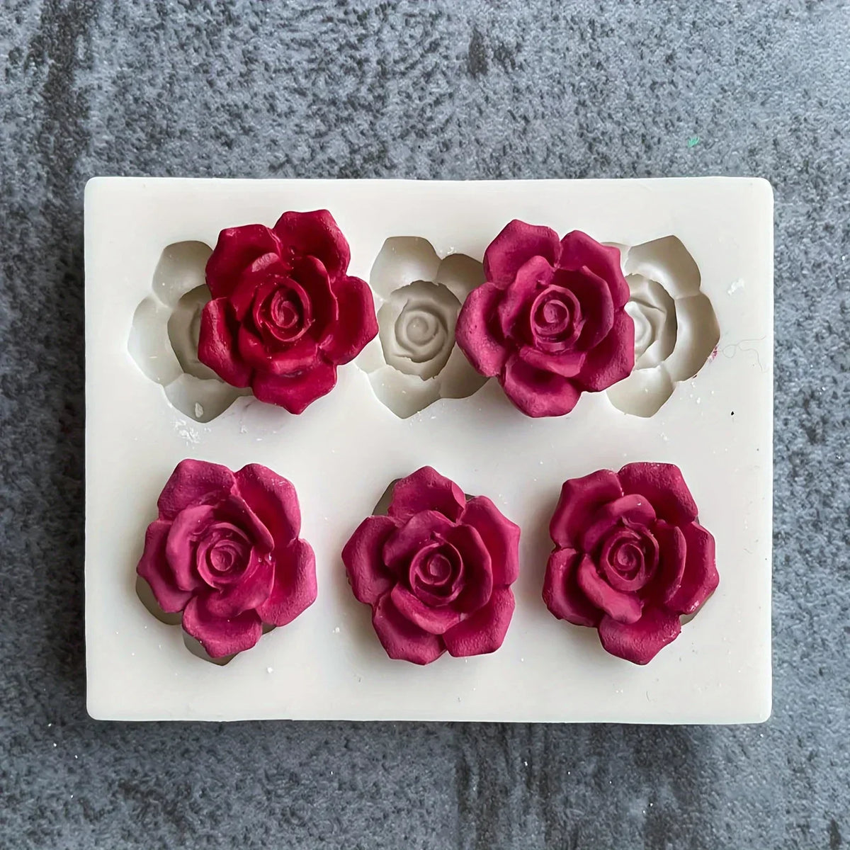 A silicone mold with five pressed rose flower shapes in shades of pink and gray for candle and soap making.