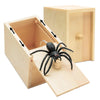 A wooden prank can containing a realistic black spider model and a small wooden chip.