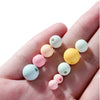 A hand holds several matte acrylic round beads in various pastel colors like pink, yellow, and mint green.