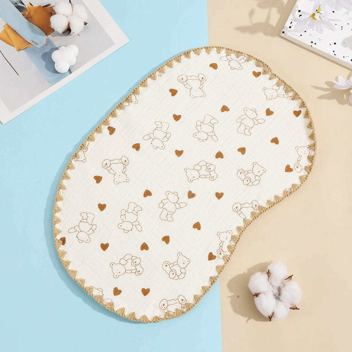 A cream-colored embroidered flat pillow with small bear and heart motifs, displayed on a light blue surface.