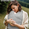 A woman gently holds a baby wrapped in a knitted fabric multi-functional baby carrier outdoors.