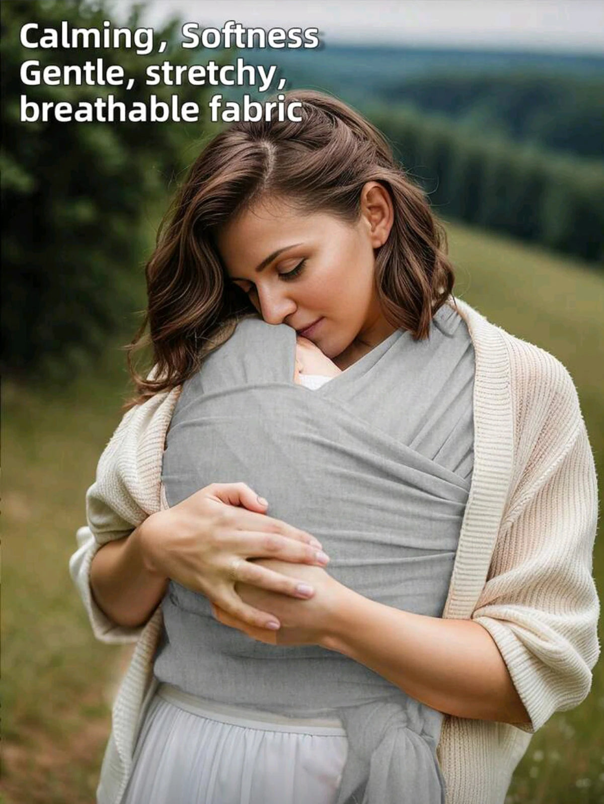 A woman gently holds a baby wrapped in a knitted fabric multi-functional baby carrier outdoors.