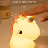A hand is tapping a cute unicorn silicone LED night light, which illuminates with a warm light.
