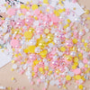 A colorful mix of pink, yellow, and iridescent resin rhinestone pearls scattered on a light wooden surface.