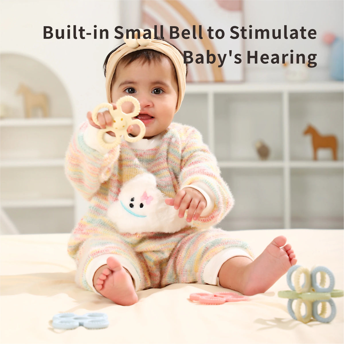 A baby is holding a silicone teether set for babies, which includes a rattle and chew toys.