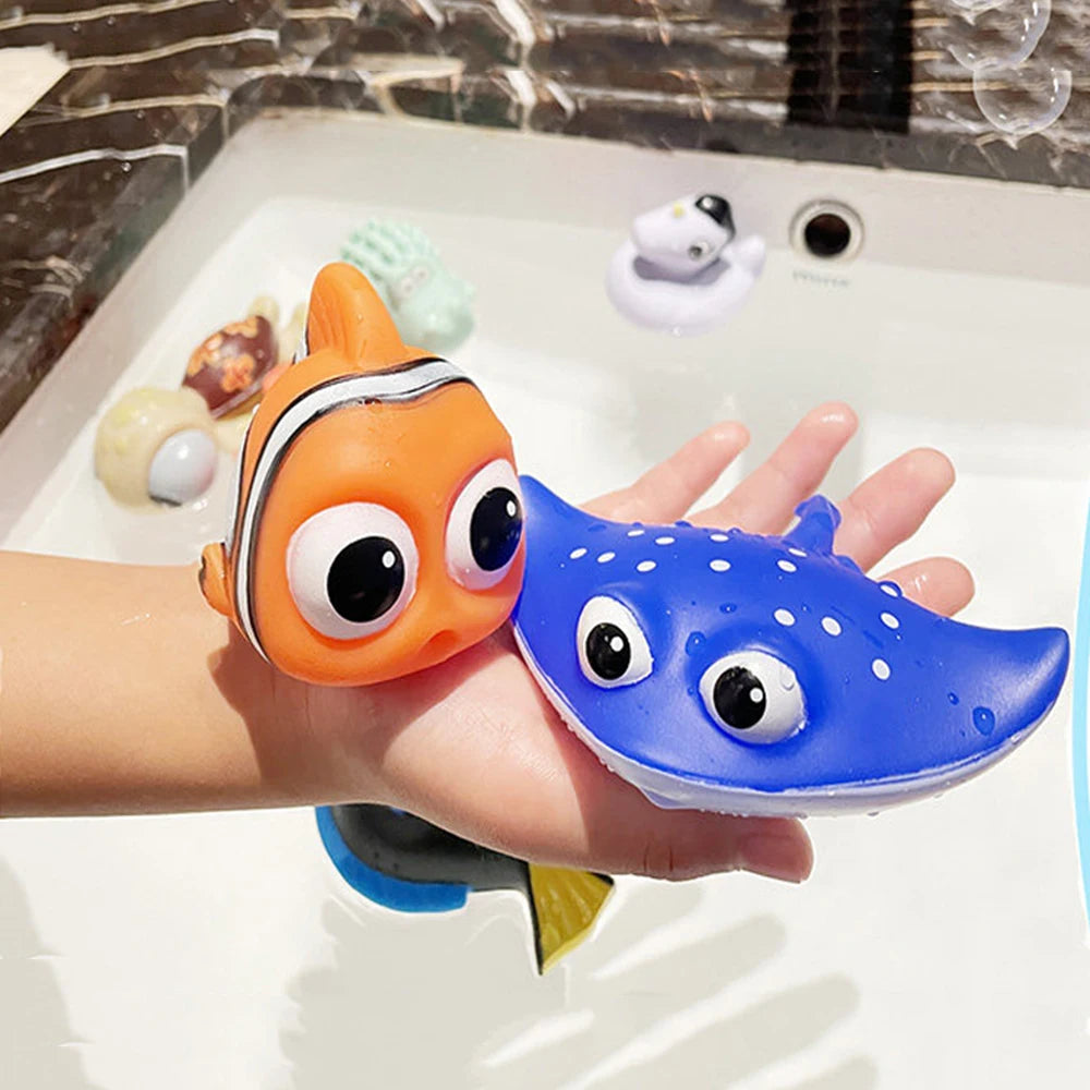 A hand holds two soft rubber bath toys, an orange fish and a blue fish, floating in water.