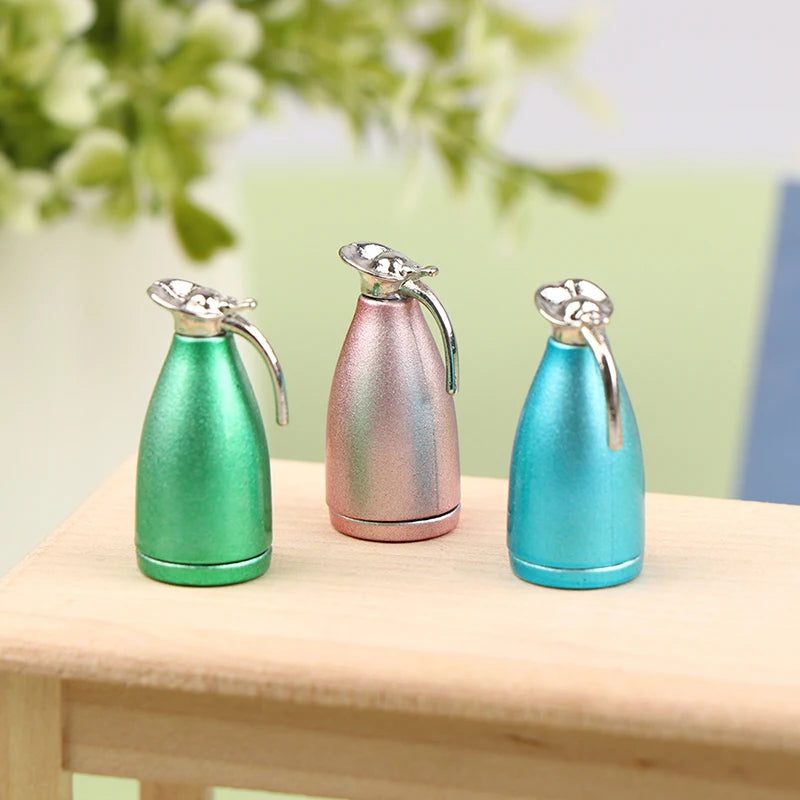 Three miniature alloy kettles in green, pink, and blue standing on a wooden surface.