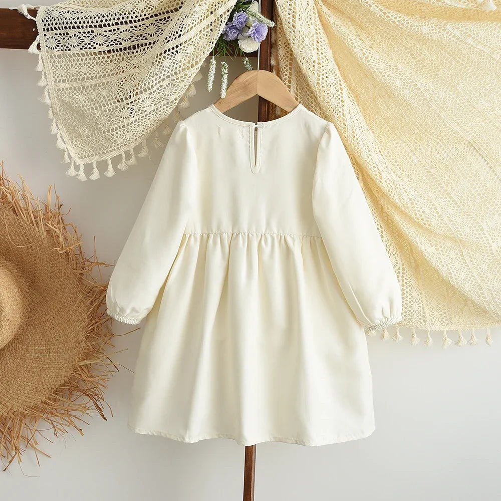 A cream-colored girls' long sleeve A-line dress with a bow detail hanging on a wooden hanger.