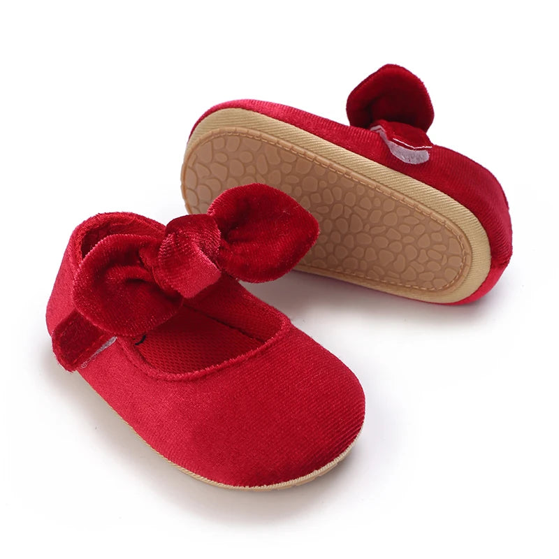 A pair of red lace-trimmed baby girl moccasin shoes with bows and tan soles.