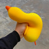 A hand is squeezing a bright yellow, squishy duck fidget toy with an orange beak and foot.