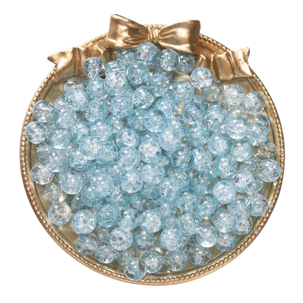 A round gold-rimmed dish filled with small, light blue glass crackle beads for jewelry making
