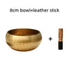 A hammered copper bowl and a leather stick are shown together for meditation or sound therapy.
