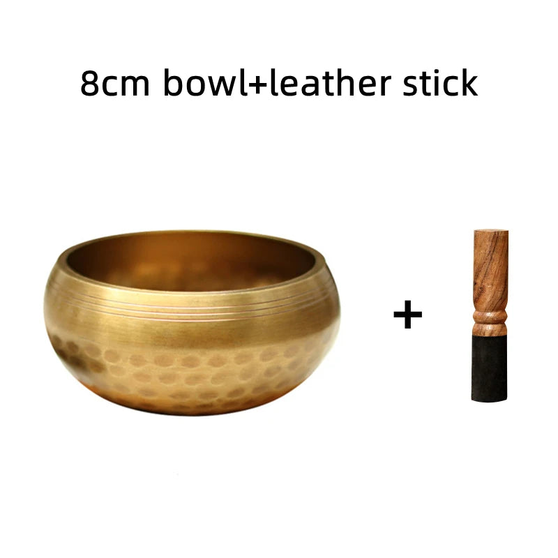 A hammered copper bowl and a leather stick are shown together for meditation or sound therapy.