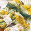 A stack of three skeins of gradient acrylic yarn in yellow, green, and white are shown draped over a surface.
