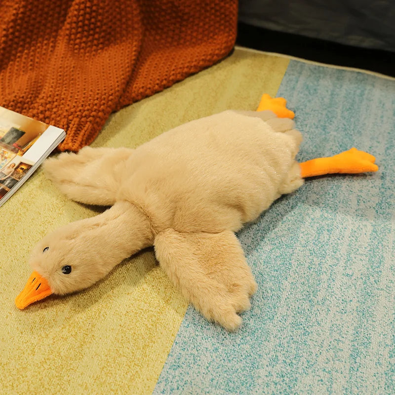 A light tan oversized kawaii goose plush pillow with orange accents resting on a pastel blue surface.