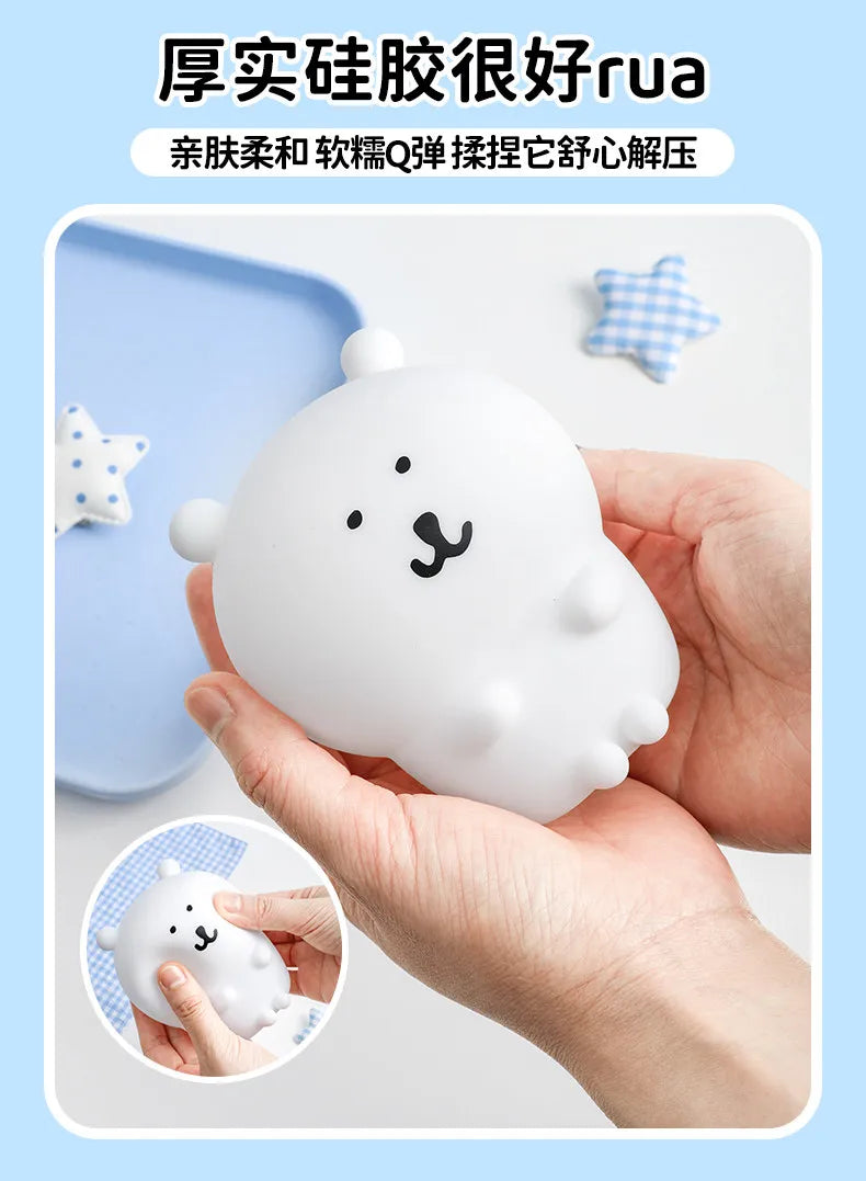 A hand holds a white silicone bear lamp with a smiling face, next to small checkered star shapes.