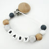 A beaded pacifier clip featuring natural wood and white silicone beads spelling out BABY.