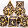 A set of seven metal dice featuring skull and dragon designs in gold and black tones.
