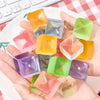 A hand holds various translucent colored ice cube squishy fidget toys on a white plate.