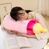 A person is resting their head on a pink plush pillow shaped like a milk bottle, with a yellow cushion attached, next to an o