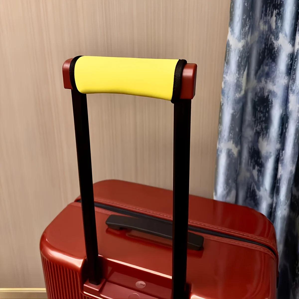 A close-up of a red suitcase handle with a yellow cushioned grip and black frame.