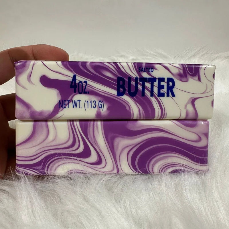 A rectangular purple and white marbled butter stick fidget toy is shown against a white fluffy background.