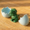 A green wind-up bouncing chick toy sits next to two white, shell-shaped molds on a wooden surface.