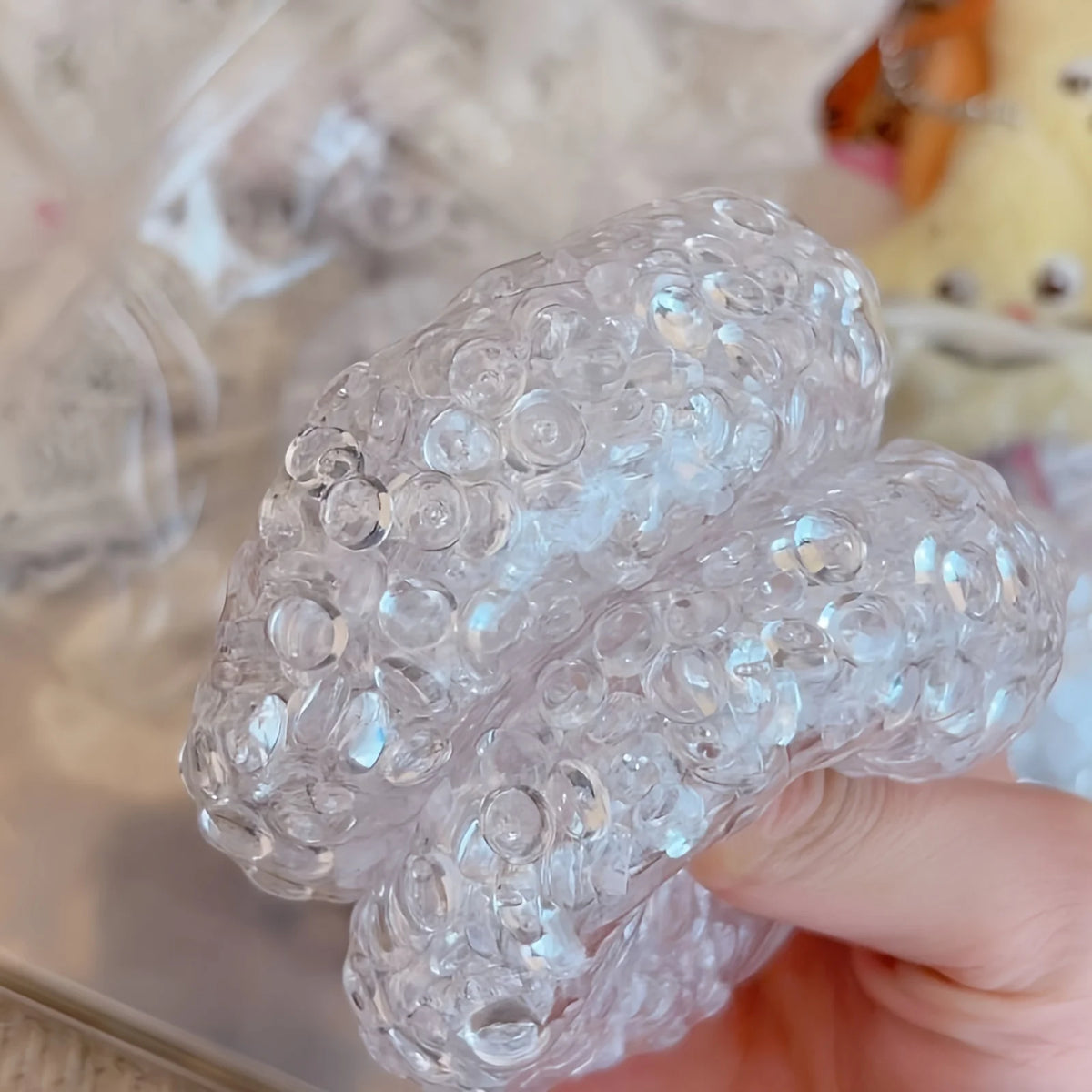 A hand holds a clear, squishy silicone fidget ball shaped like a mochi, used for stress relief.