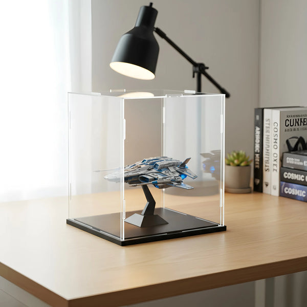 A clear acrylic display box for collectibles sits on a wooden desk under a black adjustable lamp.