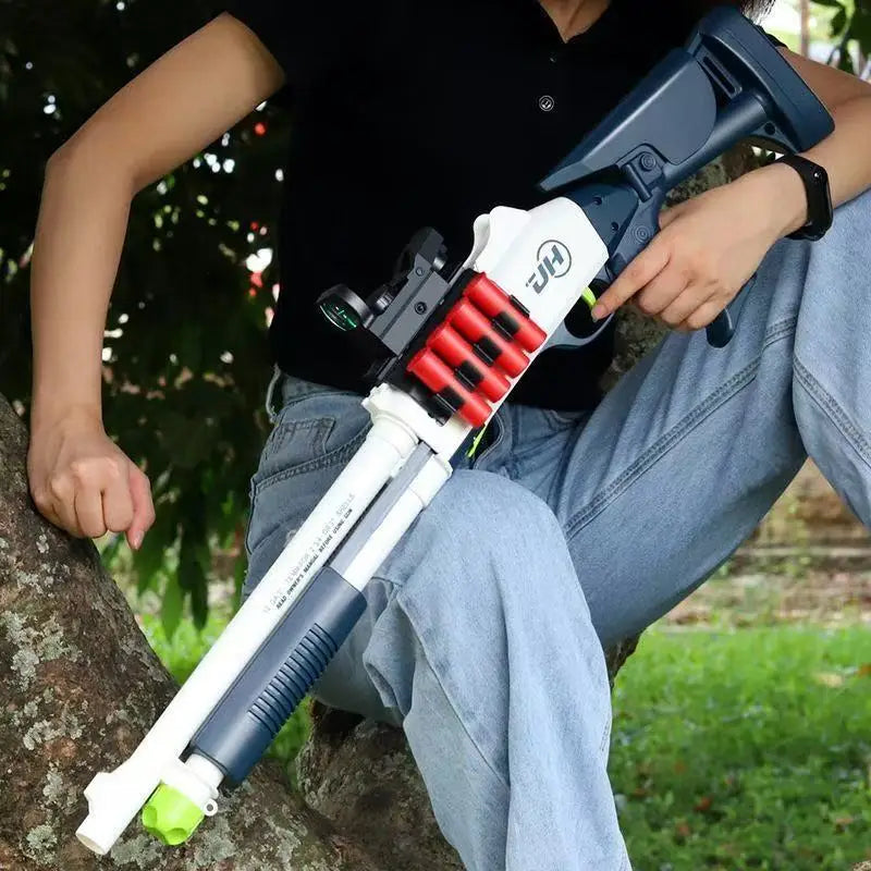 A person holds a white and black soft bullet shotgun toy with an ejecting shell action against a tree trunk.