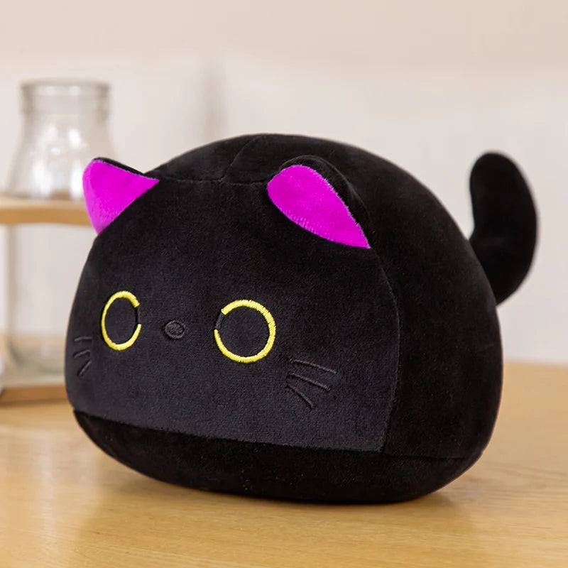 A round black cat plush toy with purple ears and yellow eyes sitting on a wooden surface.