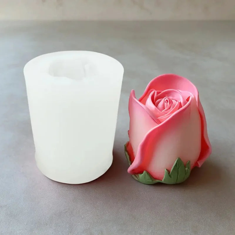 A pink rose silicone candle mold next to a white pillar candle on a gray surface.