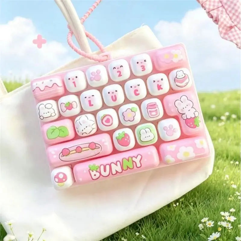 A pink and white cartoon animal keyboard keycap set is displayed in a white fabric bag outdoors.