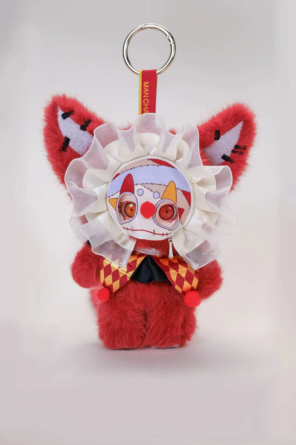 A red plush doll with white facial features and a large white frill, hanging from a silver ring.