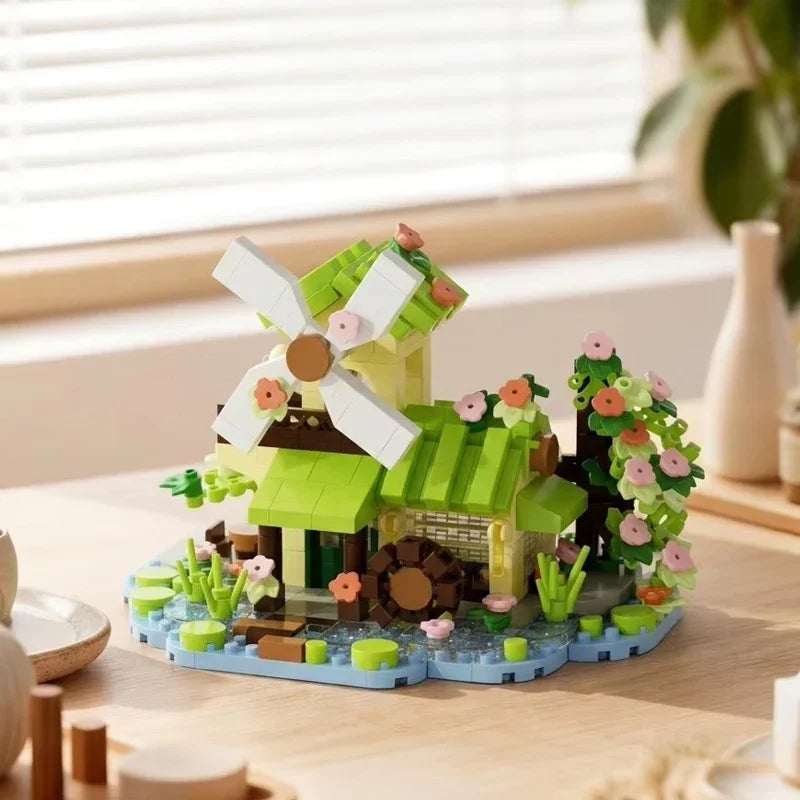 A miniature wooden building set depicting a green cabin with a white windmill and surrounding greenery.