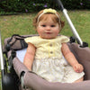 A baby doll with blonde hair and a yellow dress is seated in a stroller.