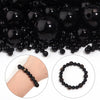 A close-up of black round imitation pearl beads scattered on a surface, with examples of strung beads shown.